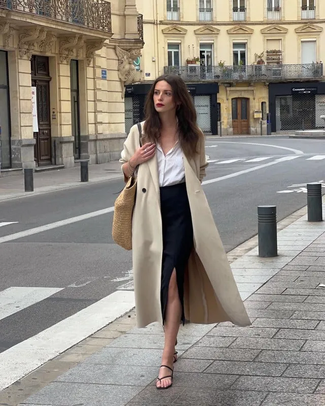 Sơ mi trắng, chân váy đen xẻ tà và áo trench coat giúp tổng thể trang phục phóng khoáng, trẻ trung nhưng không kém phần thanh lịch. 